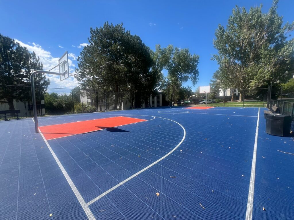 full size outdoor basketball court with blue flooring in a fenced in space