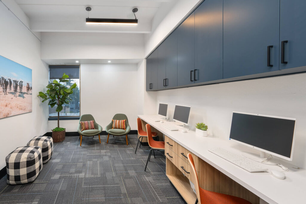 office space with long desk against a wall with computers on it and a printer