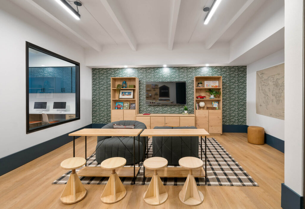 two tables with dining chairs and plush seats with television mounted on the wall and bookshelves adjacent to it