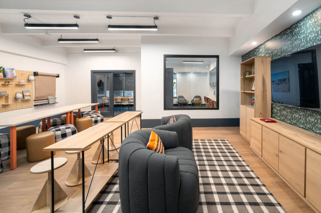tables with dining chairs and plush seats across from television mounted on the wall and bookshelves adjacent to it