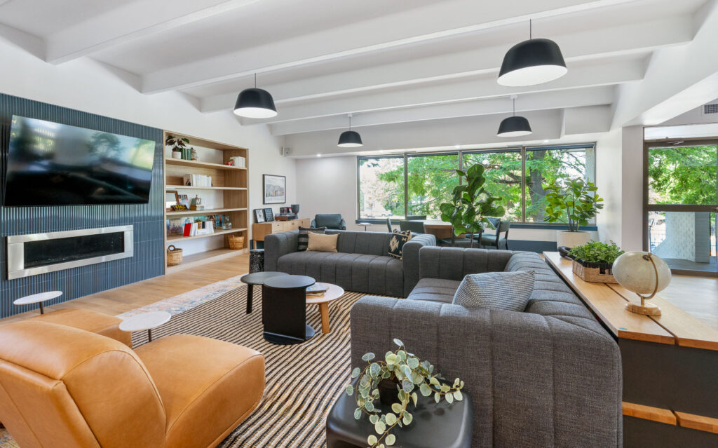 Elm at Panorama clubhouse entry seating space with sofas and armchair seating in a room with overhead and natural lighting with a television and fireplace